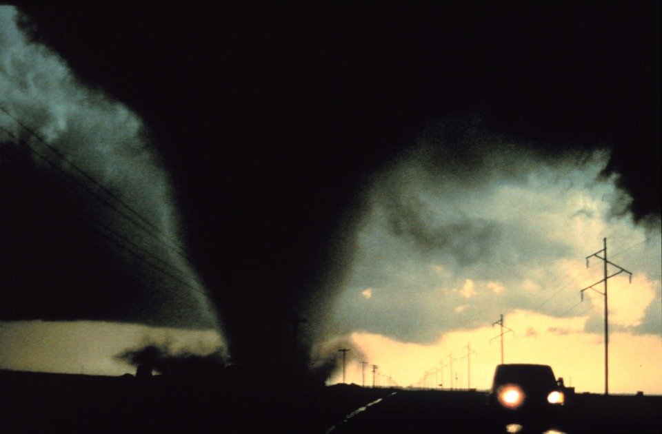 Car driving away from a very large tornado funnel cloud