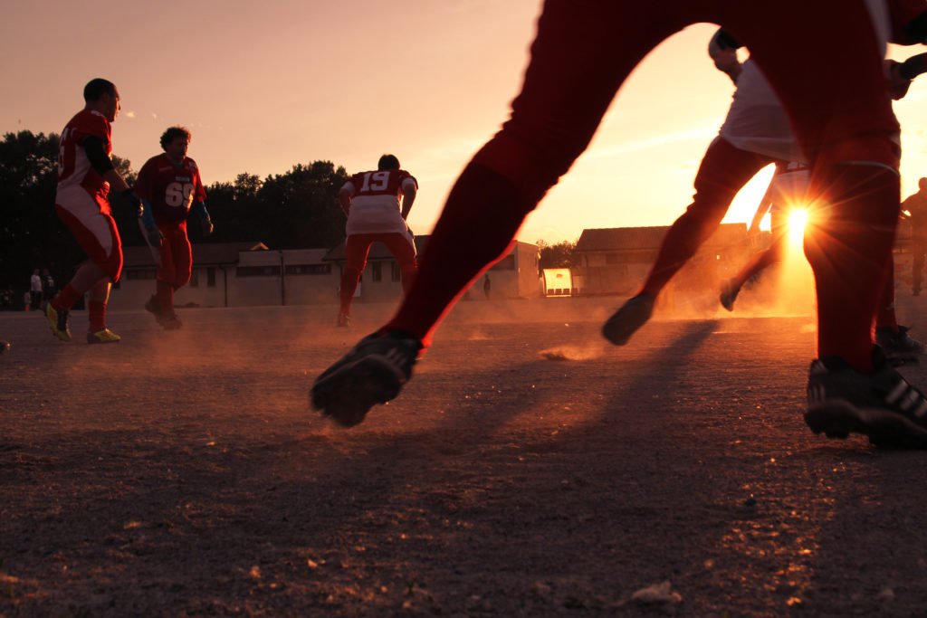 Football players practicing agility drills on a turf field as the sun rises