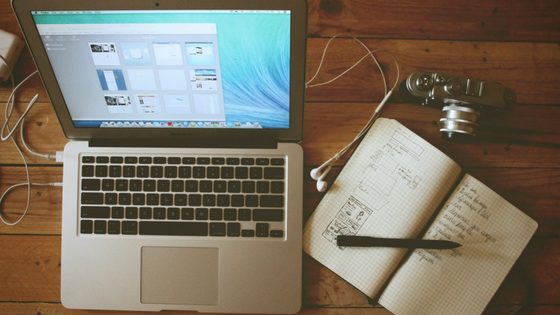A desk that has a laptop, notebook, pen, and headphones on it