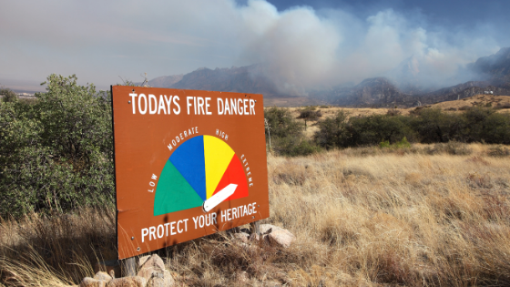 Fire danger sign in the "high" position while a wildfire burns behind it in the mountains