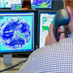 Meteorologist looking at the weather on computer screens, on the phone with a client for meteorological services 