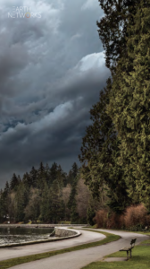 Storm clouds closing in on a nice park wit ha lake, walking path, and bench 